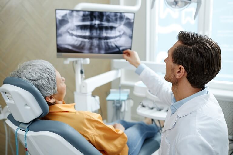 Dentista mostra panorâmica para paciente em deitado em cadeira odontológica.