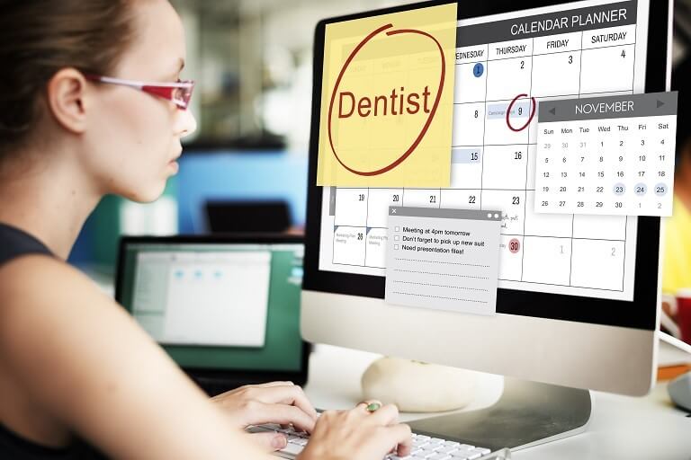 Secretária de dentista com sistema de agendamento no computador.