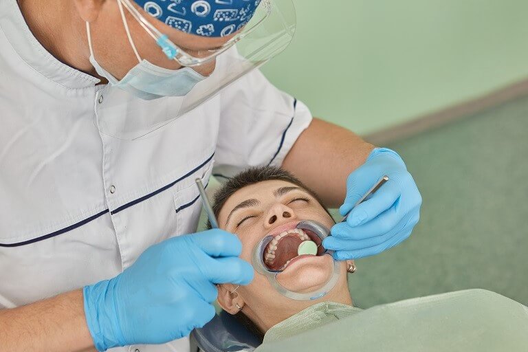 Dentista realizando procedimento em paciente com auxílio do afastador de bochecha.