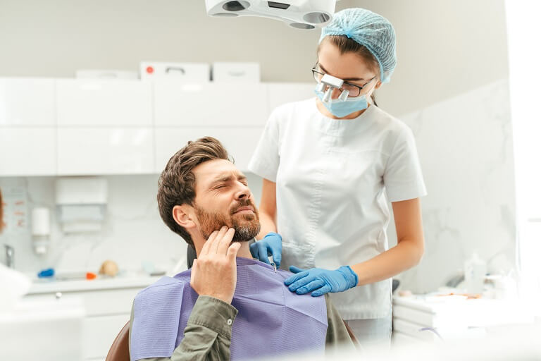 Paciente com dor de dente e mão na bochecha, sentado na cadeira de dentista.