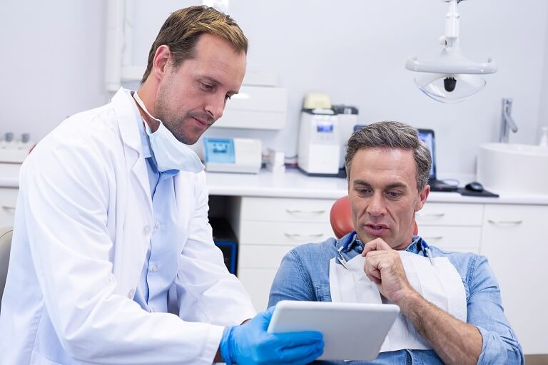 Dentista mostrando informações em tablet para paciente.